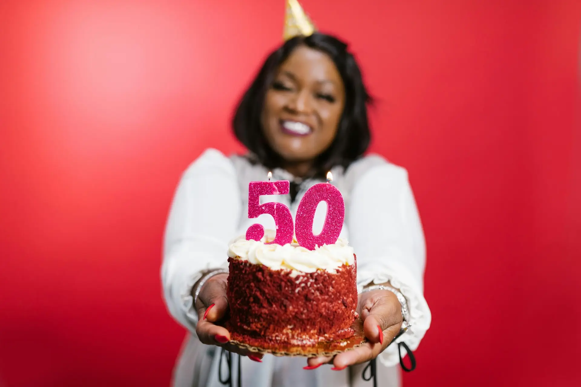 Joyful woman holding a cake with number 50 candles on a red background.