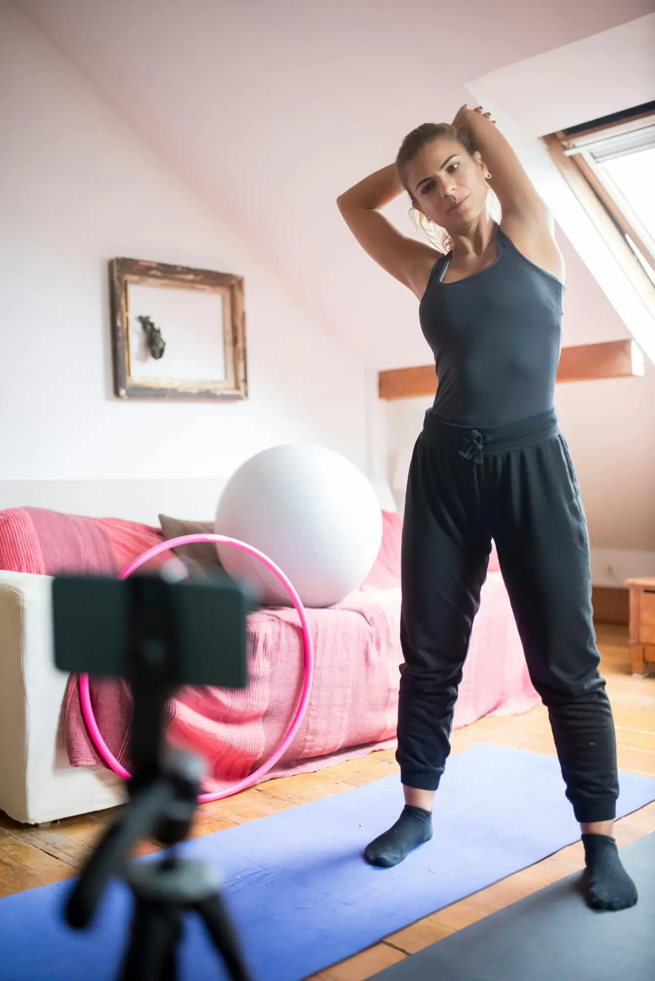 Woman in home setting stretching on yoga mat. Filming exercise for online fitness class.