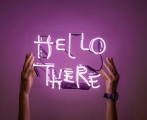 A vibrant neon sign reading "Hello There" held by hands against a purple background.